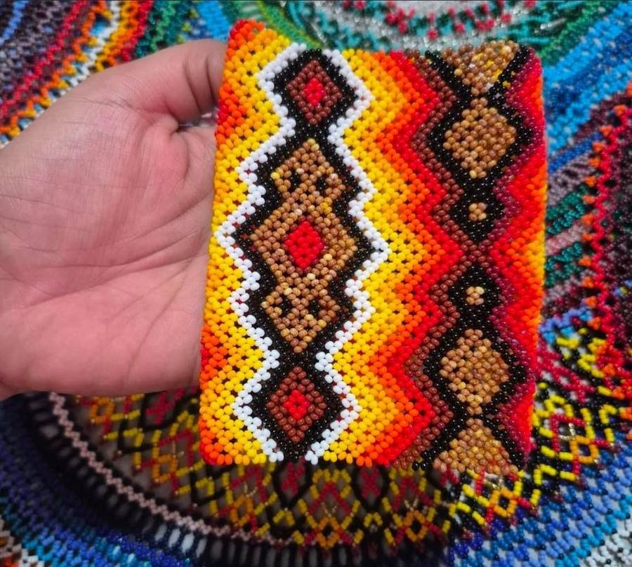 A hand holding a beaded cuff in orange, black, white and brown diamond patterns