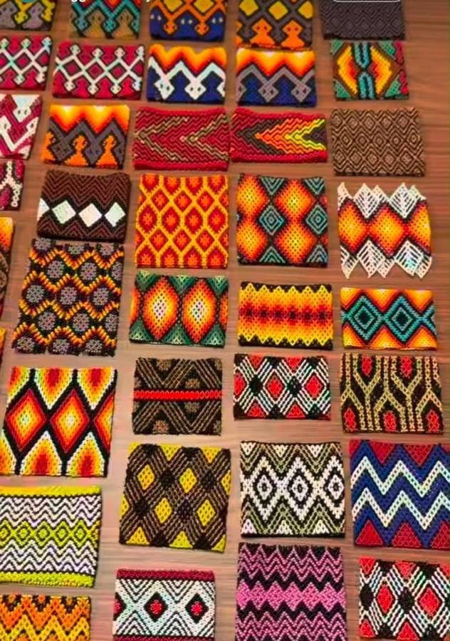 Many handmade beaded cuffs in different colours and geometric patterns laid out on a table
