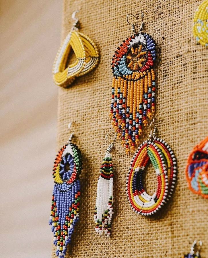 Handmade Maasai beaded earrings with fringes and discs hanging on a burlap display board