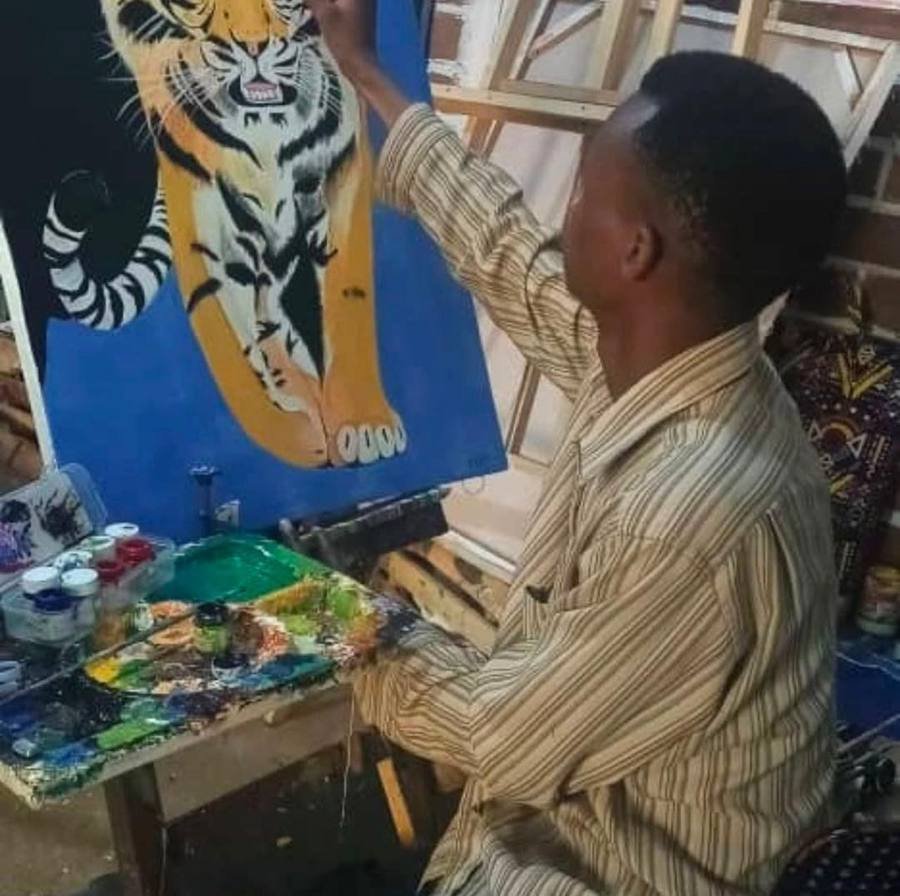 An artist painting a big cat on canvas at an easel, with paints and palette beside him