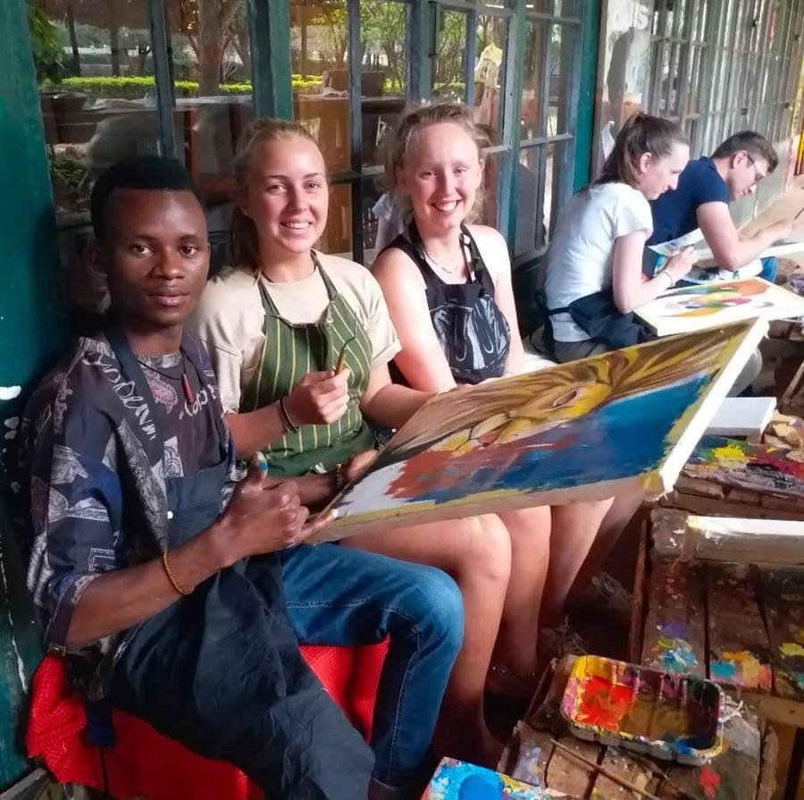 An artist holding a finished lion painting beside visitors painting their own canvases in aprons